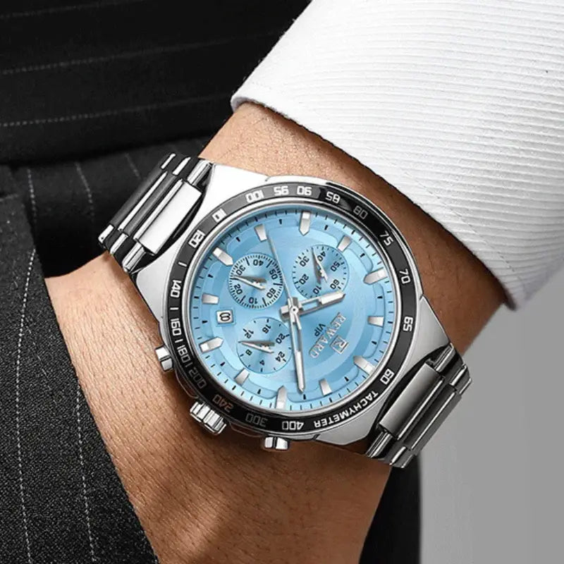 Silver watch with a blue face on a person's wrist, wearing a suit.