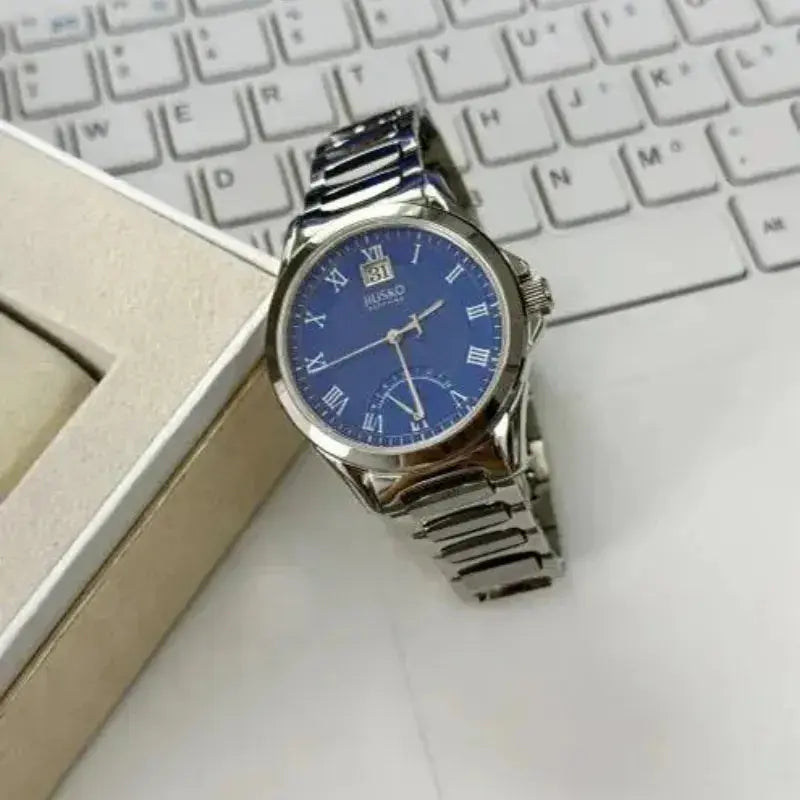 Silver watch with a blue face on a white surface next to a keyboard