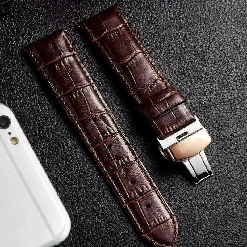 Brown crocodile-patterned watch strap on a textured surface with a phone for scale.