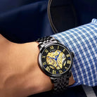 Close-up of a person wearing a black wristwatch with a blue and white checkered shirt sleeve.