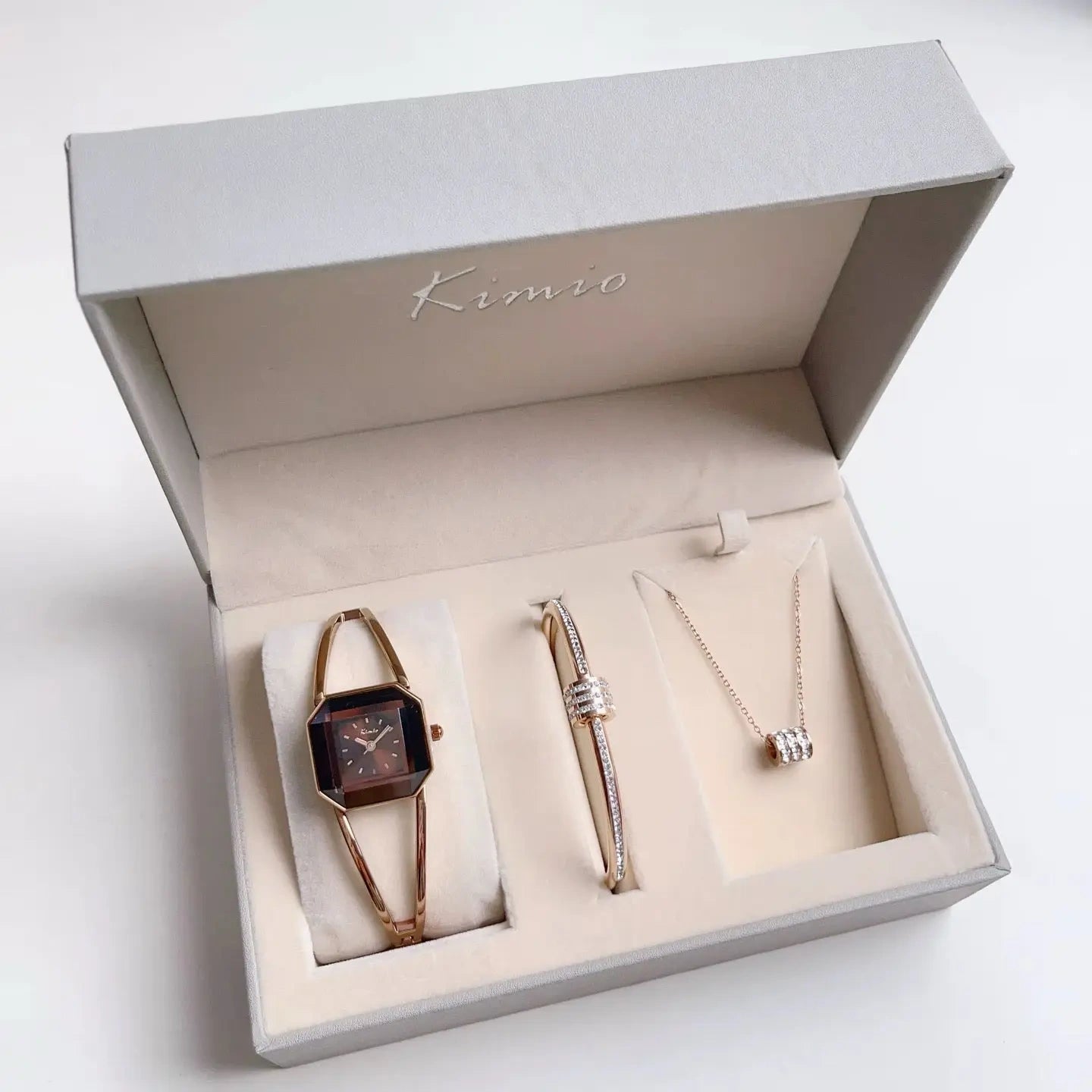 Set of jewelry including a watch, pen, and necklace in a 'Kimio' box on a white background