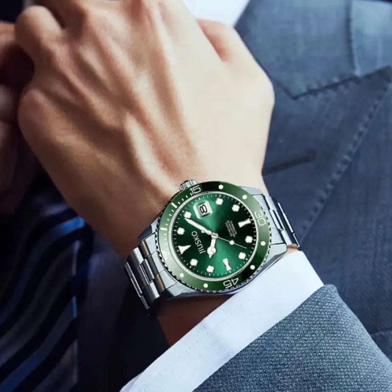 Green watch with silver case on a person's wrist wearing a suit.