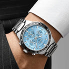 Silver watch with a blue face on a person's wrist, wearing a suit.