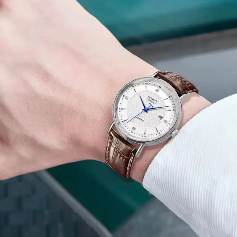 Wristwatch with brown leather strap and white dial on a wrist, blurred background
