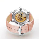 Watch with pink leather strap and visible mechanical components on a white background