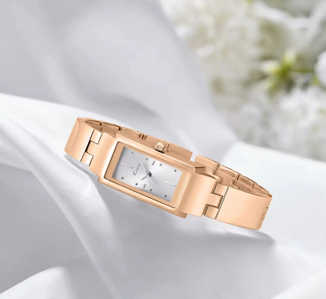 Rose gold watch on a white background with blurred flowers in the background