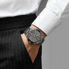 Person wearing a black watch with a detailed face on a plain background