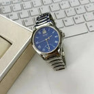 Silver watch with a blue face on a white surface next to a keyboard