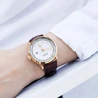 Wrist wearing a watch with a brown strap and rose gold case on a white background