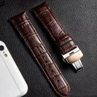 Brown crocodile-patterned watch strap on a textured surface with a phone for scale.