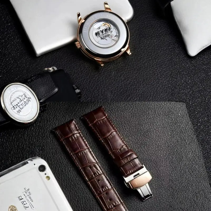 Watch with open face, brown leather strap, and smartphone on a dark textured surface
