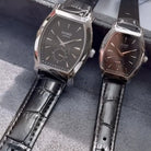 Two watches with black and brown faces and black leather straps on a gray surface.