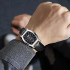 Close-up of a wrist wearing a black leather watch with a dark background