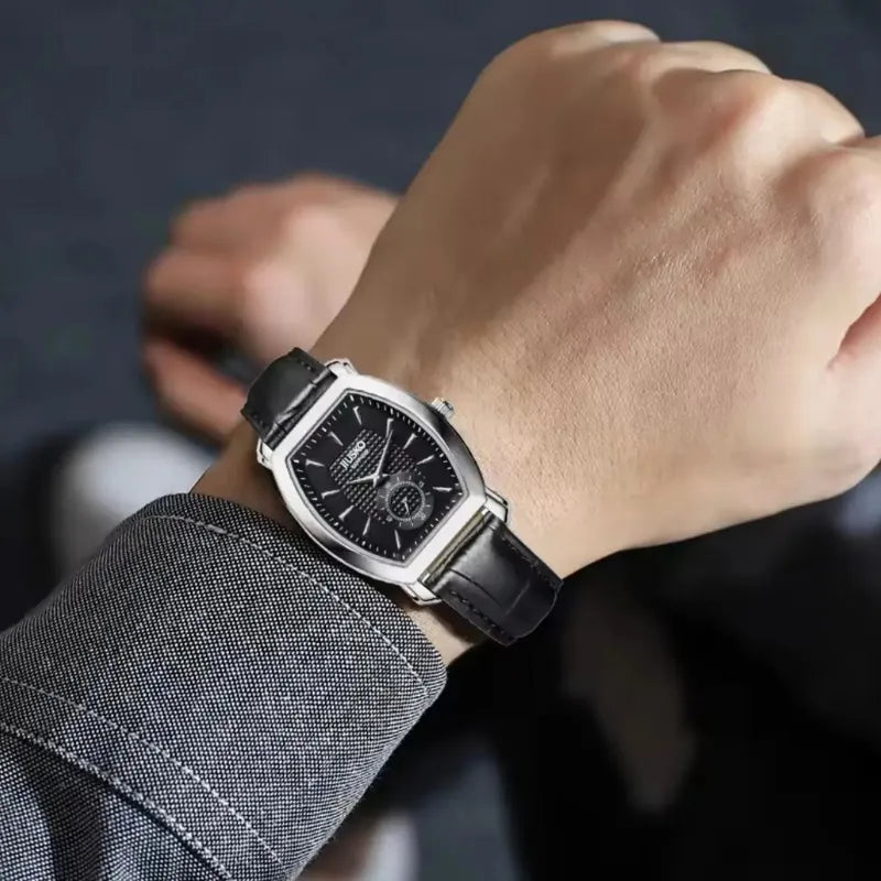 Close-up of a wrist wearing a black leather watch with a dark background